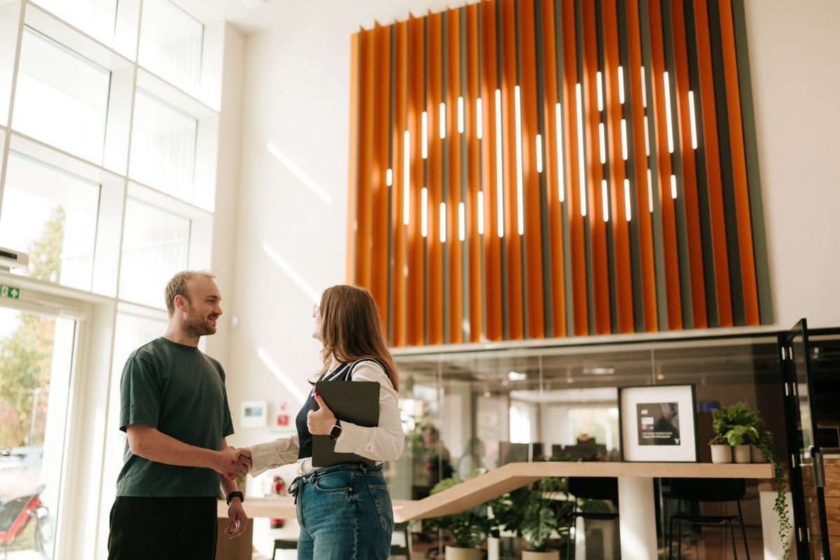 Two AE colleagues shaking hands under the orange AE logo wall
